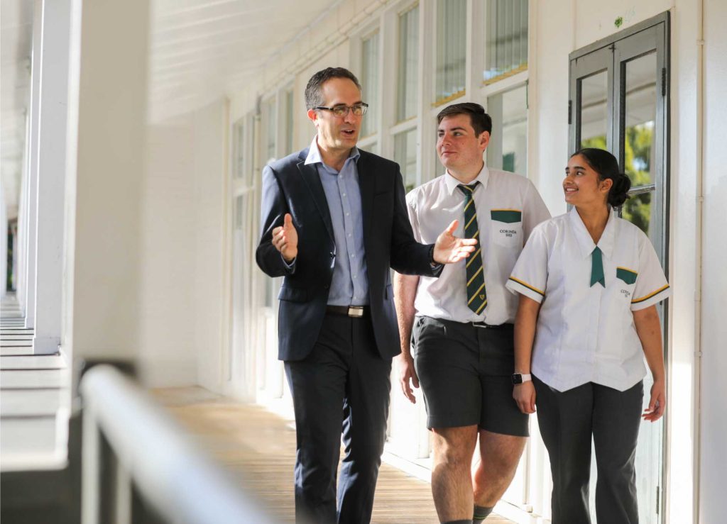 Teacher having friendly and animated discussion with two high school students as they walk down a hallway.